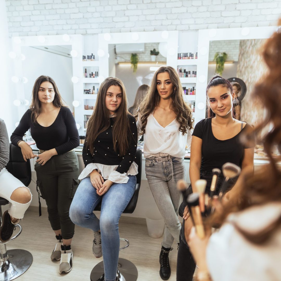 Girls are attending the make up masterclass. The educator is showing them on the model how to do glam makeup.
